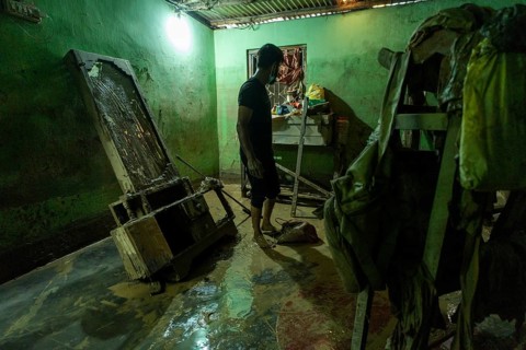 Resident walks around inside his mud-filled and flood-damaged home after floodwaters receded on