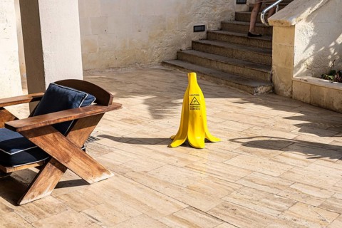 A yellow banana-shaped caution sign stands on a wooden floor. The sign warns of potential slipping