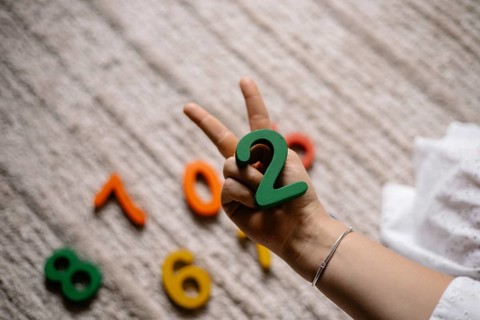 Hand showing a peace sign, holding the number two among scattered colorful numbers