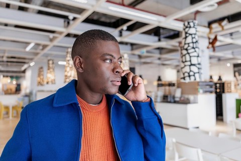 A young African man with short hair is talking on a smartphone in a modern interior space. The