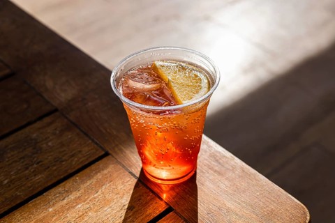 A refreshing alcohol cocktail in a clear plastic cup with ice cubes and a slice of orange. The
