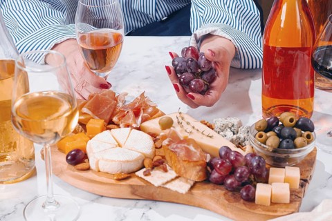 A group of friends gathers around a table enjoying drinks and a platter filled with cheese, meats,