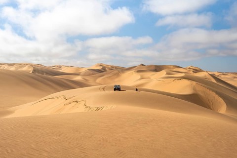 Off-road vehicle between sand dunes, sea of dunes, sandy desert, impressive desert landscape, Namib