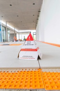 Laying tiles, in the foreground a warning sign in a construction site interior, car park