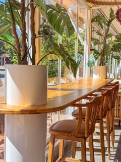 A modern restaurant interior with wooden tables and chairs. The space is bright and airy, featuring