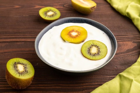 Yogurt, with kiwi in blue bowl on brown wooden background and green linen textile, side view, close