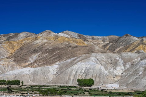 Small settlement and cultivated fields in front of mountainous landscape, erosion landscape near Lo