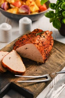 Roasted turkey breast is prepared and sliced on wooden board. In the background, there are side