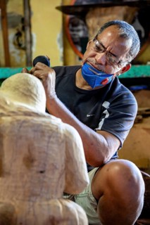 Concentrated man carving with a small tool sculpture in a studio, craftsman leg carving masks in