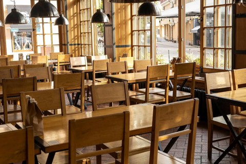 The interior of a cozy cafe features rows of simple wooden chairs and tables bathed in warm,