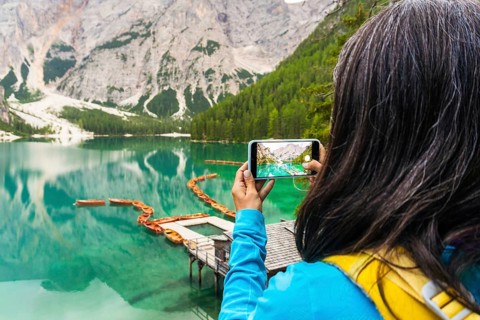 Woman hiker taking smartphone landscape photo of Lago di Braies Lake in italian Dolomites mountains