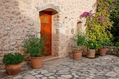 Rustic stone façade with wooden door and decorative flower pots in the courtyard, Majorca, Balearic