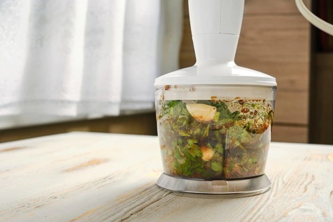 Kitchen mixer chopping fresh herbs and garlic with soy sauce and olive oil. Food processor on a