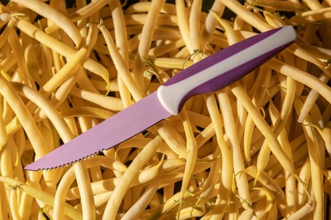 A purple knife is lying on a heap of yellow beans