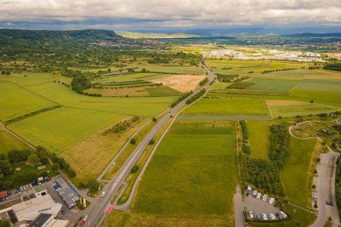 Landscape with a country road and numerous fields surrounded by hills under a cloudy sky,
