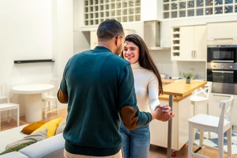 Cheerful young couple dancing and holding hands in their bright modern home, sharing a loving,