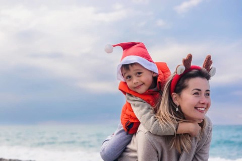 A mother and her young son enjoy a winter day at the beach. The mother has brown hair and wears a