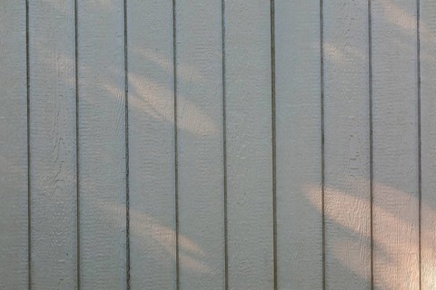 Close-up of light grey painted vertical Canexel wood plank cladding on garden shed wall with