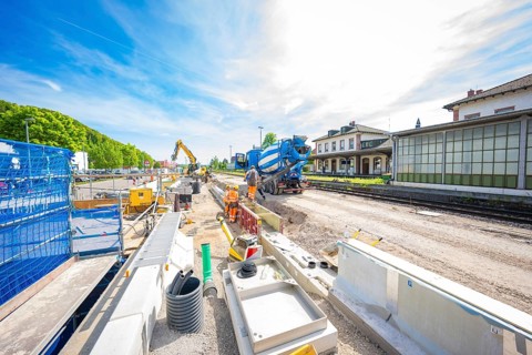 Wide-angle view of a construction site with excavator and building materials under a blue sky,
