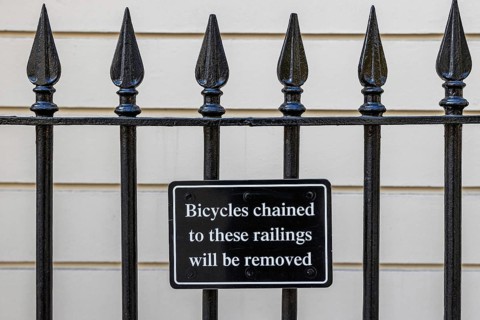 A black wrought iron railing bears a sign warning that bicycles chained to it will be removed