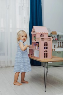 A young girl in a striped dress engages with a colorful dollhouse, smiling happily indoors
