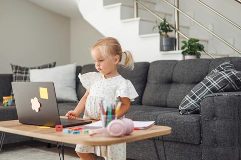 Young blond European girl using laptop at table with colored pencils and headphones in modern