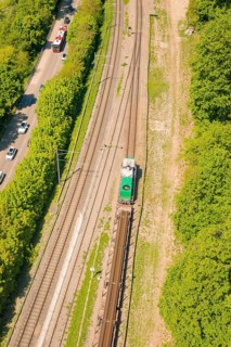 Close-up of a railway line with a passing train, next to it road and vegetation, construction site