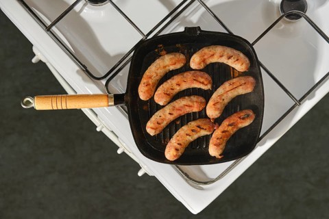 Top view of banger sausages in cast iron skillet placed on stove in kitchen. Grill marks are