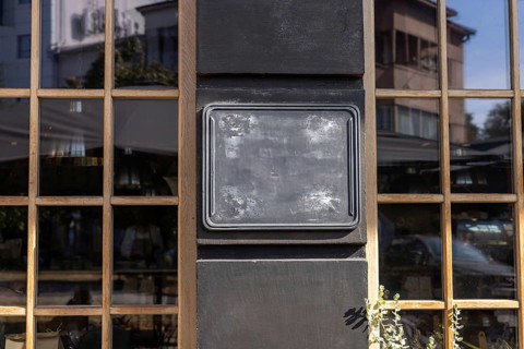 A black blank chalkboard sign is displayed on the exterior wall of a restaurant, illuminated by the
