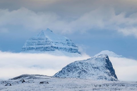 Large rock behind clouds cover one of the three mountains Tee Kroner, Kongsfjord or Kongsfjorden,