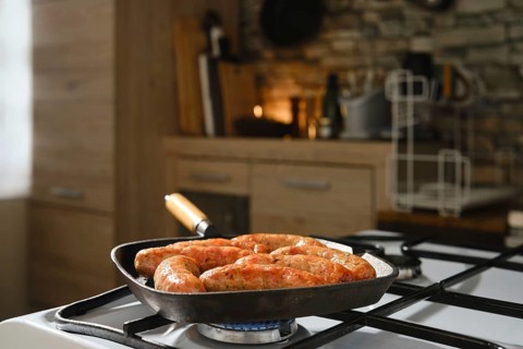 Homemade sausages in cast-iron skillet on gas stove. Grilling banger sausages in griddle pan at