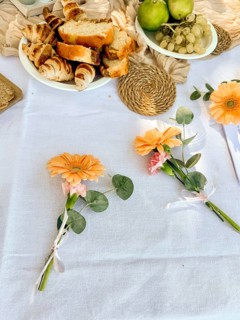 A table setting with fresh flowers, bread, and fruits. The scene includes orange flowers, green