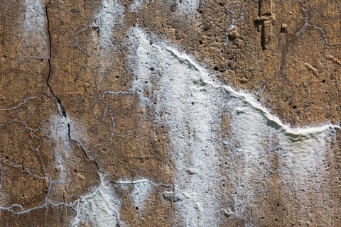 Close-up of cracks in damaged concrete surface with some cracks filled and repaired with white