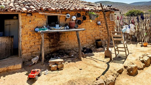 Rustic outdoor kitchen with clay walls and kitchen utensils on one wall, houses in a village in the