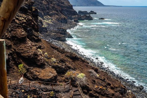 Couple walking path along rugged coastline with dark volcanic cliffs meeting the turquoise atlantic