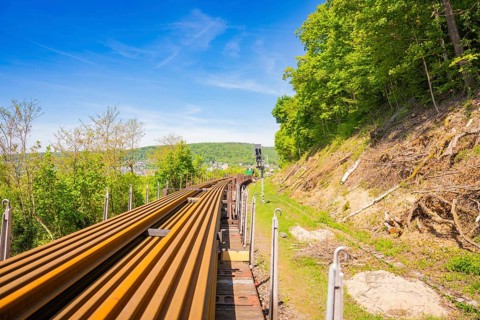 Rails run along a hill with forest under a clear blue sky, Leonhard Weiss construction site to