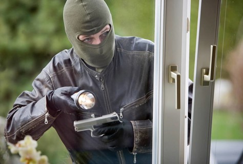 A burglar with flashlight and pistol, breaking into a family home, studio shot, Austria