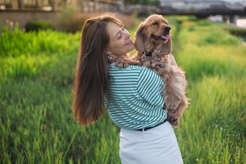 A woman holds her happy dog while standing in a field near mountains
