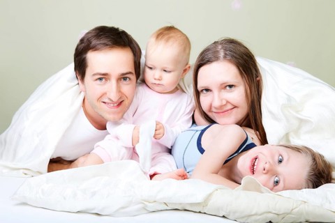 A young happy family, four people relaxing in bed, Finland, Scandinavia