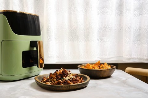 Air fryer sits on table with two wooden bowls nearby. One bowl contains roasted chanterelle