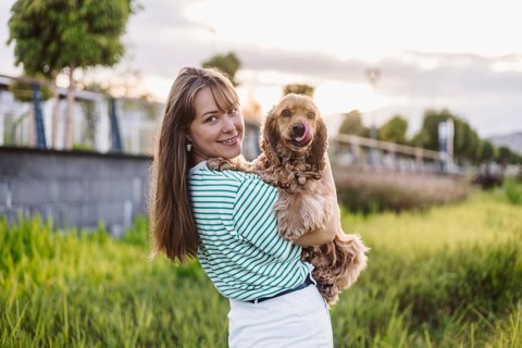 A woman holding a dog in a park during sunset, both appear cheerful