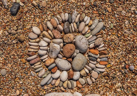 A circular arrangement of smooth pebbles on a sandy surface. The stones vary in size and color,