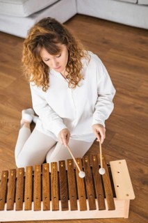 Woman playing a xylophone on a hardwood floor, focused and concentrated