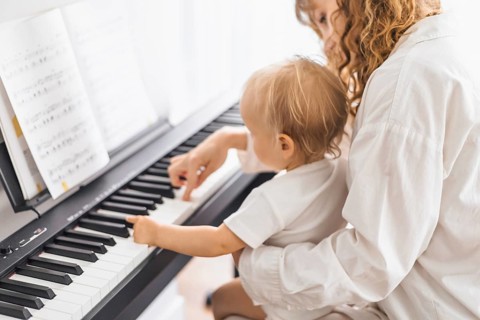 A woman guides a toddler exploring piano keys, fostering a learning environment