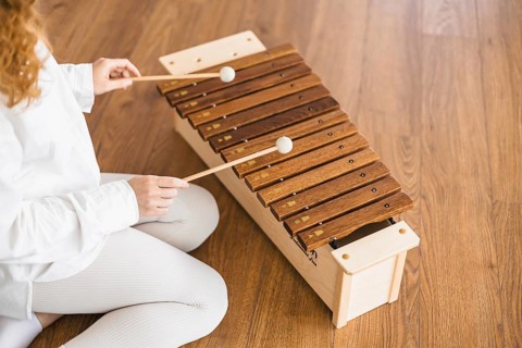 Woman playing marimba with focus, sitting on a wooden floor