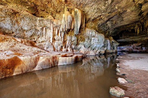 Reflective water surface in a cave with dramatic stalactites and rock formations, The Gruta do