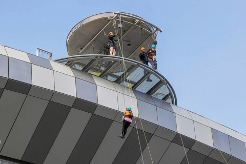 Three harnessed abseilers descend ropes from the circular viewing tower at Tottenham Hotspur