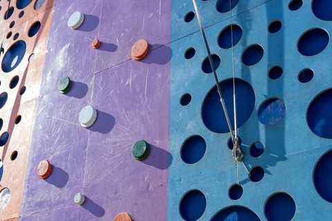 Tackling a colorful tall climbing wall tower. The setting offers a fun and engaging outdoor