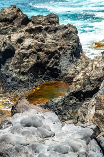 Jagged volcanic rock formations creating a natural pool with orange hued nutrient rich water,
