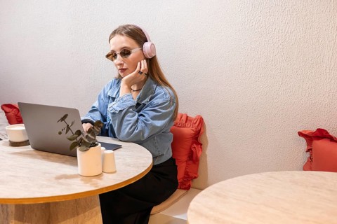 Young Caucasian woman with long blonde hair wearing pink headphones and sunglasses, working on a